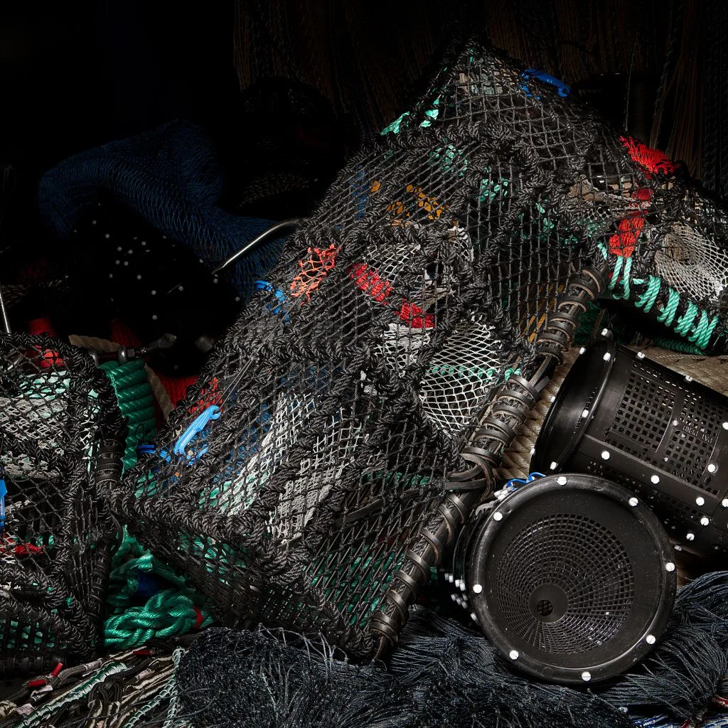 A large pile of stacked lobster pots and creels, featuring durable mesh, ropes, and bait bags, ready for use in inshore fishing operations.