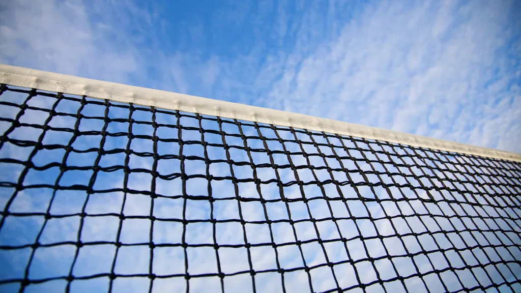 A high-quality tennis net stretched across a standard tennis court under a clear blue sky.